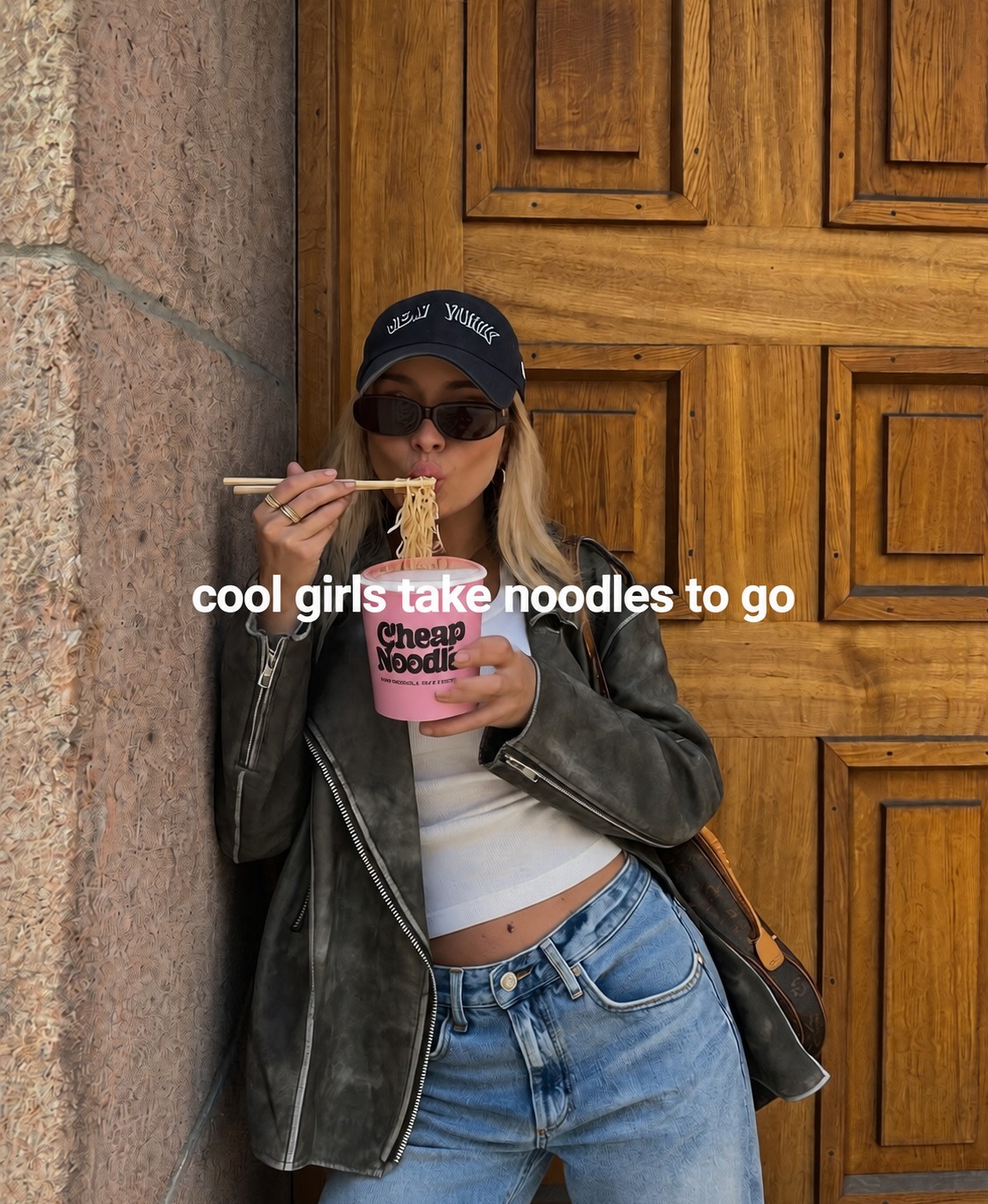 Woman in a cap and sunglasses eating noodles from a pink cup